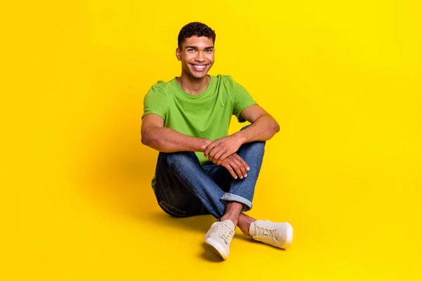全长照片 迷人而快乐的男人穿着绿色T恤坐在地板上 微笑着孤零零的黄色背景 — 图库照片
