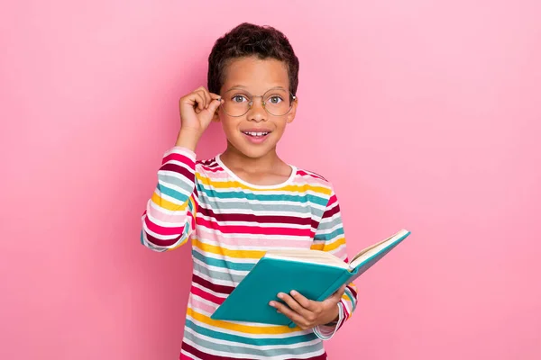 甜美聪明的学童深色头发的照片 穿着条纹长袖 手持书本 用粉色背景隔绝的手触摸眼镜 — 图库照片
