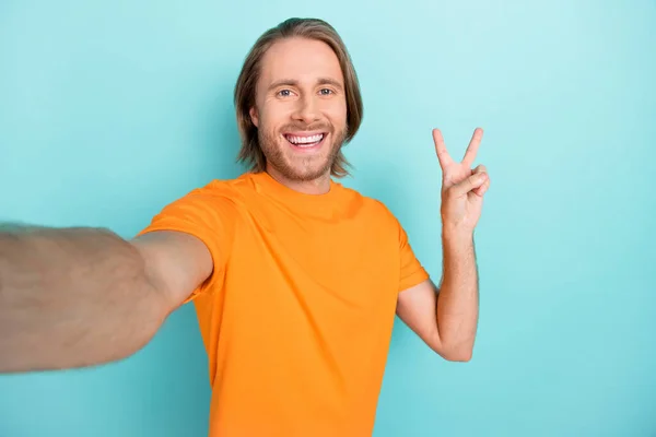 一个心情好的男人穿着橙色T恤自拍视频 显示V字形孤立的绿松石色背景 — 图库照片