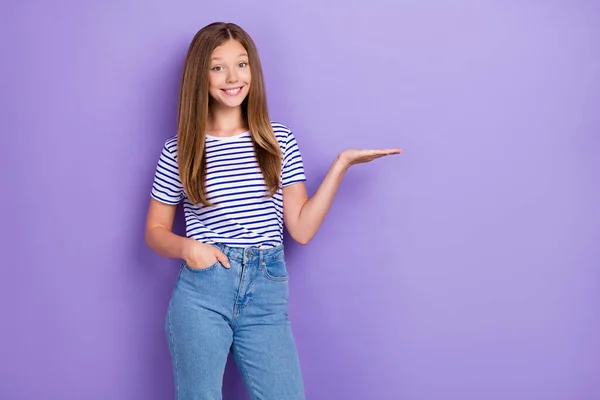 ポケットパームの中にストライプのTシャツの腕を身に着けている愛らしい満足した女の子の写真紫色の背景に隔離された空のスペースを示す — ストック写真