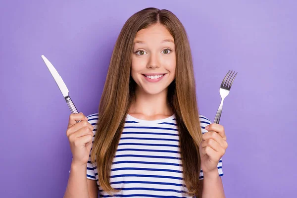 お腹を空かせた女の子の写真ストレートヘアドアはストライプTシャツホールドスプーンナイフおいしい食べ物紫色の背景に隔離された — ストック写真