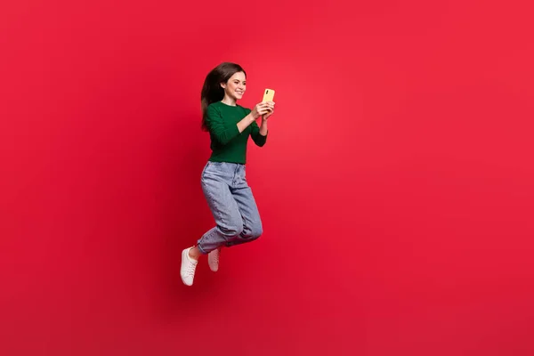 미디어를 이용하여 점프하는 쾌활하고 소녀의 사진붉은 배경에 고립된 — 스톡 사진