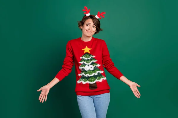 Photo of cute funky lady wear red sweater looking horns hair band shrugging shoulders isolated green color background.