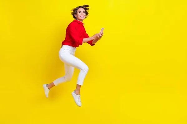 興奮したスポーティーな女性ジャンプホールド使用電話ラン孤立した上の黄色の色の背景 — ストック写真