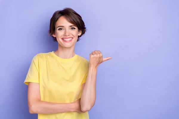 若い魅力的なかわいい女性のクローズアップ写真は 黄色のTシャツの指ポイントを身に着けています空のスペースおもちゃの笑顔広告紫色の色の背景に隔離された — ストック写真