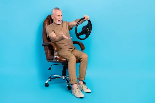 Full size portrait of mad confused person hand hold wheel sit chair isolated on blue color background.
