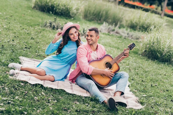 两个年轻学生情侣坐在公园草地上弹奏吉他手的照片 — 图库照片