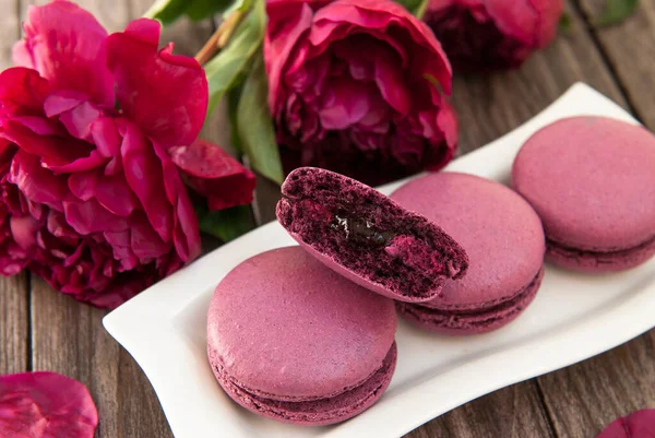 Macaroons stuffed with currants, purple peonies on wood background