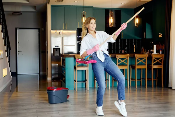 Beyaz gömlekli ve kotlu mutlu kadın evi temizlerken eğleniyor, paspası gitar gibi düşün.