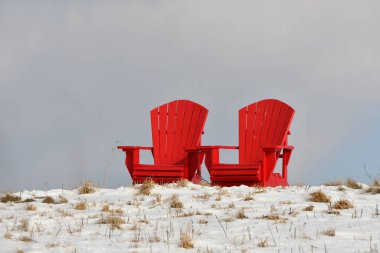 Kış sahnesi karla kaplı tepede iki kırmızı sandalye.