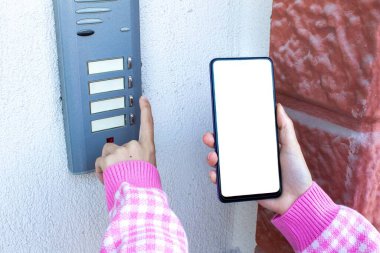 Kadın kapı zilini çalıyor ve elinde boş beyaz masaüstü ekranlı cep telefonu var. Cep telefonunun görüntüsü.