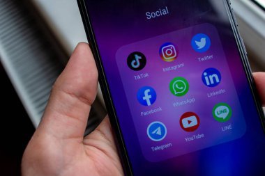Akıllı telefonu tutan adam. Sosyal medya uygulamaları (TikTok, Instagram, Twitter, Facebook, WhatsApp, LinkedIn, Telegram, YouTube, Line) ekranda simgeler.