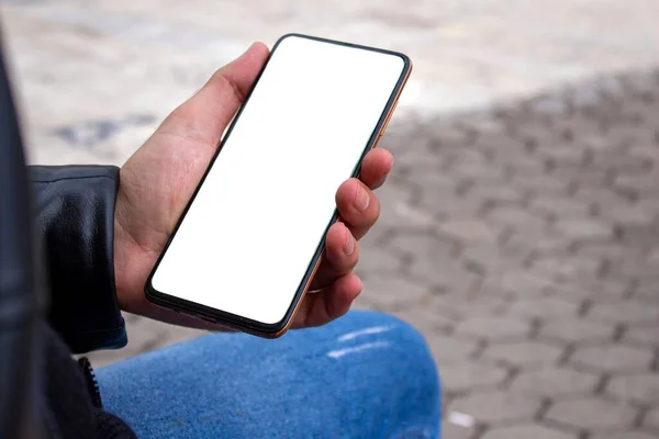 公園に座っている間 白い画面の携帯電話を持っている男 手にスマートフォンのモックアップ画像 — ストック写真