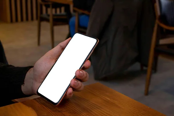 カフェに座りながら白い画面のスマホを持っている男のモックアップイメージ 携帯電話のコピーを手に — ストック写真