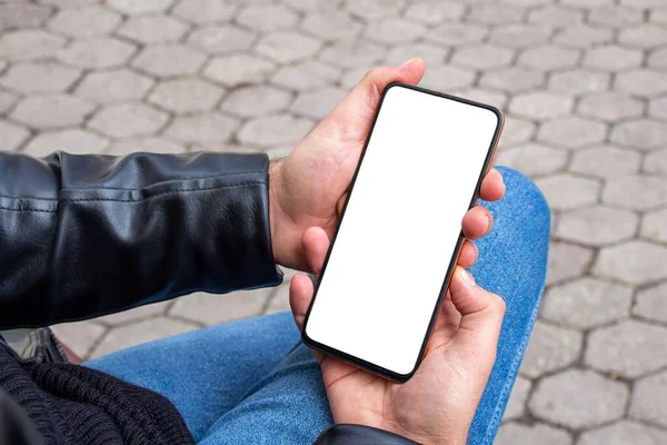 公園に座っている間 白い画面の携帯電話を持っている男 手にスマートフォンのモックアップ画像 — ストック写真
