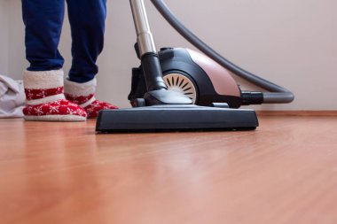 Kadın parke zeminini temizlemek için elektrikli süpürge kullanıyor. Çok fazla toz olan evi temizliyor..