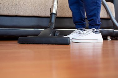 Kadın parke zeminini temizlemek için elektrikli süpürge kullanıyor. Çok fazla toz olan evi temizliyor..