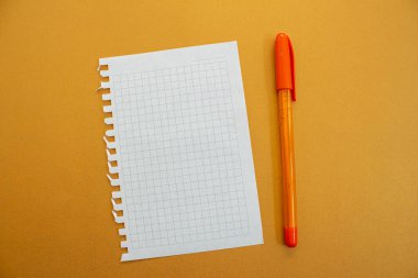 Sarı arka planda boş defter kağıdı ve kalem izole edilmiş. Üst manzara, düz uzanma.