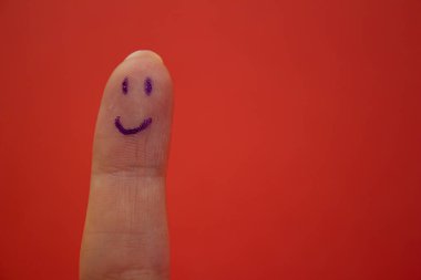 Kırmızı arka planda izole edilmiş parmak üzerine gülen yüz çizilmiş. Mutluluk ve gülümseme kavramı.