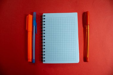 Boş bir defter ve kırmızı arka planda izole edilmiş bir kalem. Üst manzara, düz uzanma.