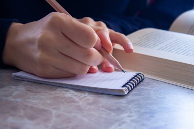 Öğrenci evdeki masada ders çalışıyor. Not defterine not alan bir kadın.