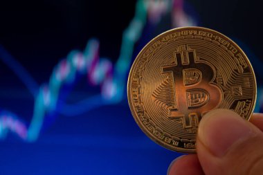El ele tutuşan bitcoin, arka planda bulanık borsa grafiği. Kripto para birimi yatırım konsepti. Boşluğu kopyala.