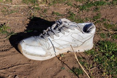 Doğaya atılan eski bir spor ayakkabı. Çevre kirliliği kavramı. Yerde beyaz eski bir ayakkabı.