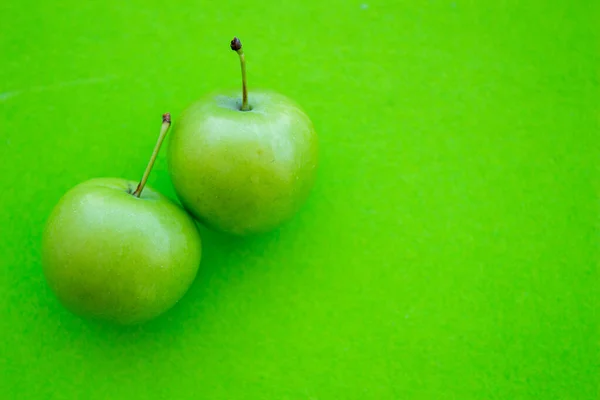 Green plums isolated on green background. Top view photo of sour plum fruits with space for text.