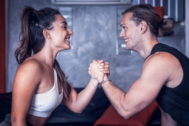 İki neşeli atletik beyaz adam oturma odasında Sqat eğitiyor. Güzel kız ve genç adam yeni stüdyo evlerinde gülümseyen bir bacak ve kalça sporu için el ele tutuşuyorlar.