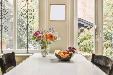 Vazoda güzel çiçekler, meyveler ve bir pencere olan yemek masası.