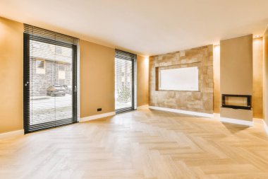 Geniş pencereli boş bir oda ve modern bir evin parke zemininde küçük bir şömine.