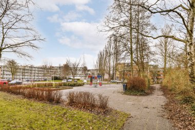 Bulutlu bir günde arka planda binaları olan ağaçlarla parktaki oyun parkı.