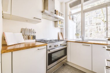 Gümüş-gri ocağı ve geniş pencereleri olan beyaz mutfak odası.