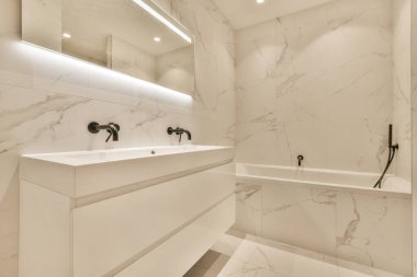 Evdeki çağdaş tuvaletteki aynanın altındaki duvarda musluk ve sıvı sabun asılı.