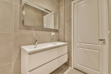 Lavabo ve aynalı dolap kapının yanındaki fayanslı duvara ve modern tuvaletteki kurutma tezgahına bağlı.