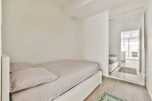 Minimalist interior design of small bedroom with soft bed placed in corner and wooden wardrobe and shelves with lamp illumination