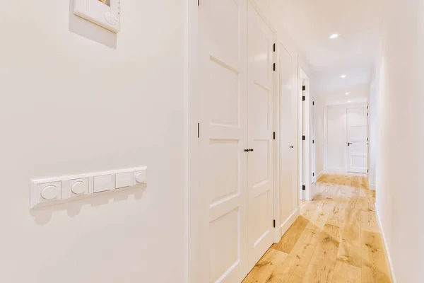 Light narrow hallway with many doors in white walls and glowing lamp over lumber floor