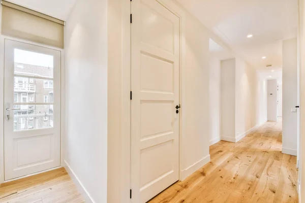 Light narrow hallway with many doors in white walls and glowing lamp over lumber floor