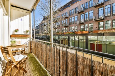 Metal parmaklıklı dar tuğla balkon, tahta sandalye ve camlı kapı mutfağa açılıyor.