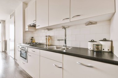 Üzerinde gümüş gri lavabo olan beyaz ahşap mutfak dolapları.