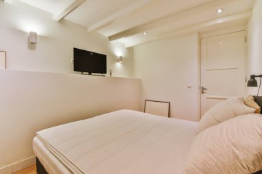 Küçük yatak odasının minimalist iç tasarımı. Köşesinde yumuşak yatak, ahşap gardırop ve lamba aydınlatmalı raflar var.