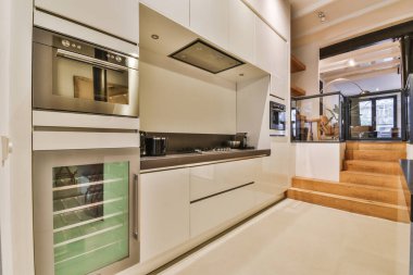 Stüdyo dairesinin modern minimalist tarzı iç tasarımı açık beyaz mutfak ve yemek masası ve sandalyeleri tavan arası lambasıyla aydınlatılmış.