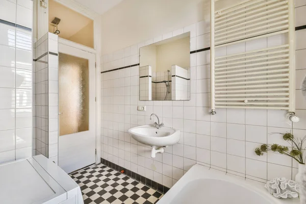 stock image Cupboard with sink and mirror attached to tiled wall near door and drying rack in modern restroom