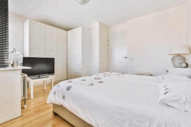 Yatak odasının içi gri yatak odası, beyaz ahşap gardırop ve televizyon.