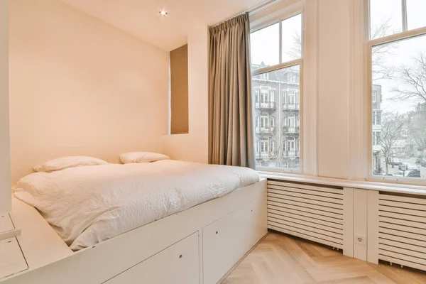 窓付きの現代的な寝室で輝くランプと額装の写真の近くに位置する快適なベッド — ストック写真