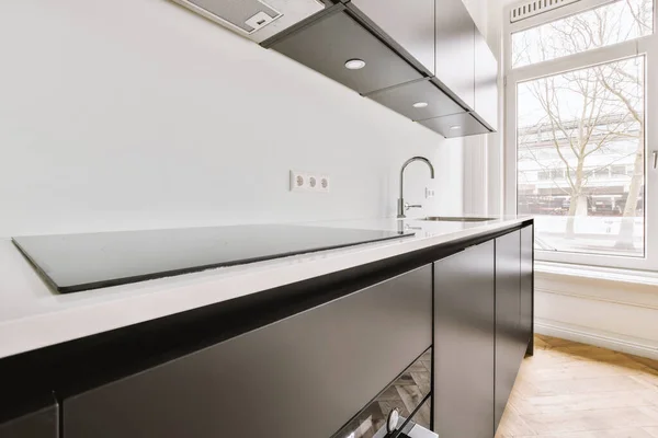 Fragment of interior of black home kitchen with minimalist style white furniture with sink and stove