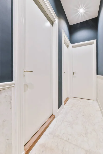 Light narrow hallway with many doors in blu walls and glowing lamp over lumber floor