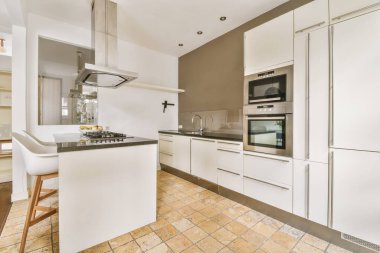 Çağdaş mutfakta dolaplara ve fırına karşı egzoz kapağının altındaki tezgahların yanına yerleştirilmiş rahat sandalyeler.