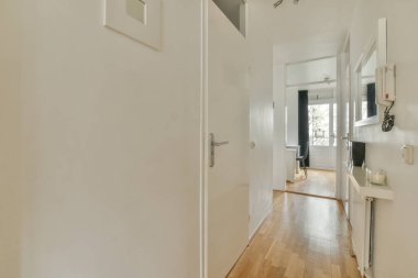Beyaz duvarları, aynası ve parke zeminli minimalist tarzı dairesi olan boş dar koridor manzaralı.