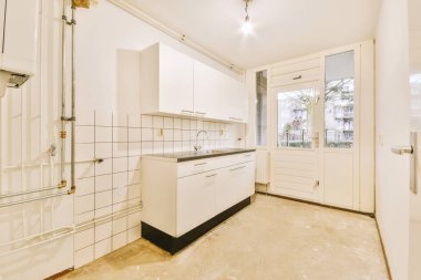 İyi organize edilmiş küçük bir ev mutfağı pencerenin altında lavabo, sobalı hafif mobilyalar ve kentsel apartmanda buzdolabı var.